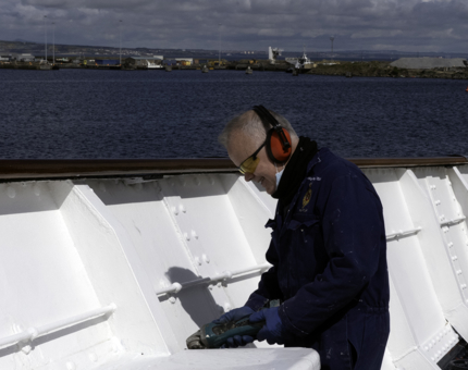 A man treating rust spots on the Fo'c’s’le Deck.