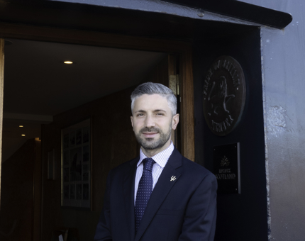 A man wearing a suit standing by the front door of Fingal. 
