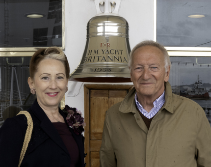 A couple standing next to The Royal Yacht Britannia's Bell. 