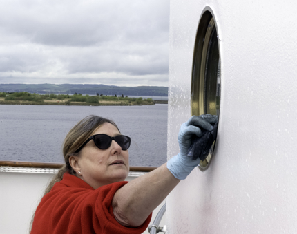 A woman from Housekeeping is polishing a porthole.