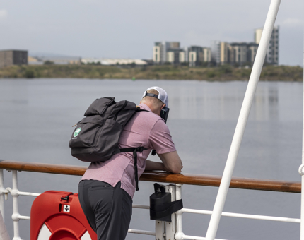 A visitor listens to the audio guide while leaning over a handrail on deck. 