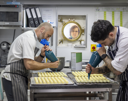 Two Pastry Chefs are filling petits fours in the Galley. 
