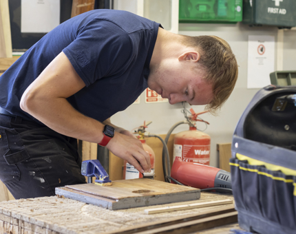 A member of the Maintenance team in the workshop removing varnish from a handrail.