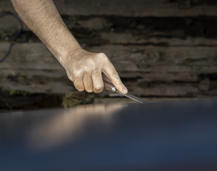 A man is preparing for painting by removing old filler on the starboard hull.