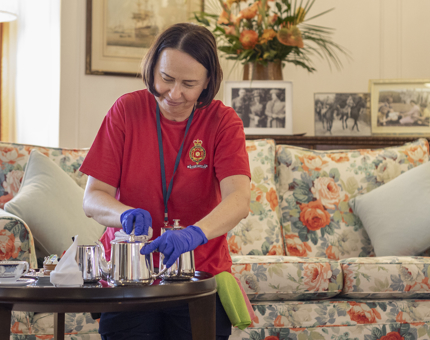 A Housekeeper is polishing a silver teapot on a table in the State Drawing Room. 
