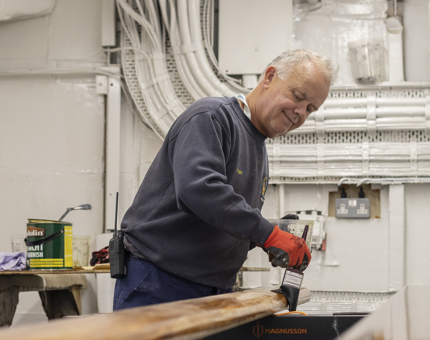 A man holding a paintbrush varnishing a handrail.