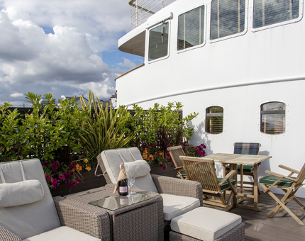 A table with chairs and two deck chairs outside on the deck of a ship. 