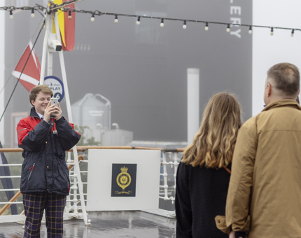 A Visitor Assistant taking a photo of two visitors on the Verandah Deck.