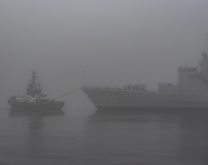 A boat towing a ship from the harbour in the fog.