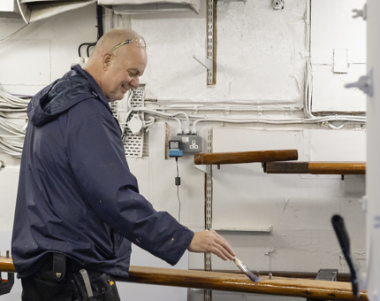 A man holding a paintbrush holding a paint brush, varnishing a handrail. 