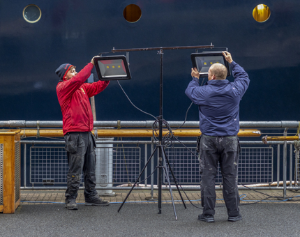 Two men standing next to the ship installing a freestanding light fixture. 