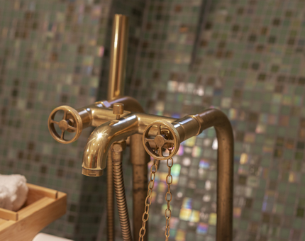 A close up of brass taps with a green tiled wall behind.