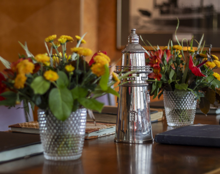 Yellow and red flowers, and a silver lighthouse ornament decorate a wooden table. 