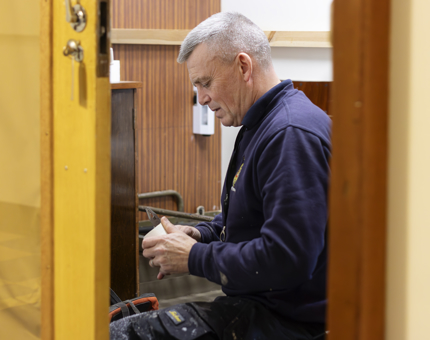 A man in a blue jumper fixing a pipe. 