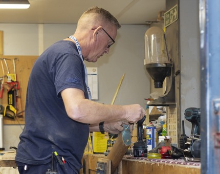 A man standing at a workbench fixing a brass end to a handrail. 
