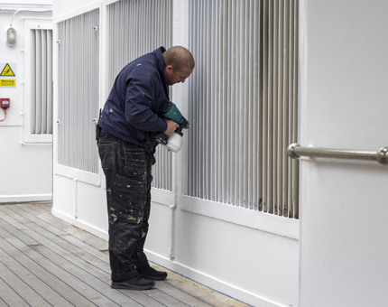 A man wearing a blue top and trouser painting a wall white. 