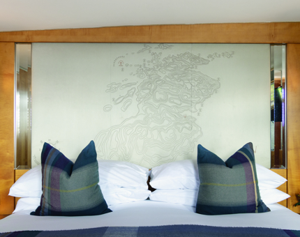 A closeup of a headboard with a map of Scotland on it. There are four white pillows with two tartan ones in front.