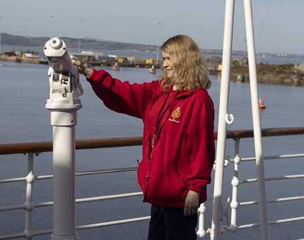 A woman in a red jumper cleans a white telescope on Britannia's deck. 