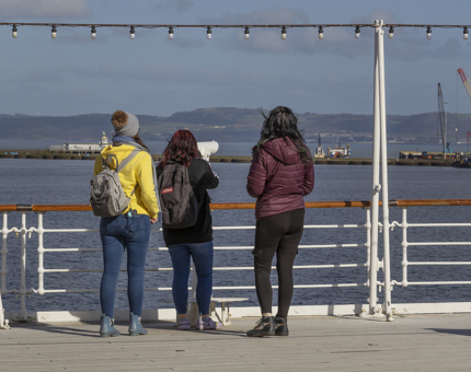 Three women look at the views across the water with a telescope on the Verandah Deck. 