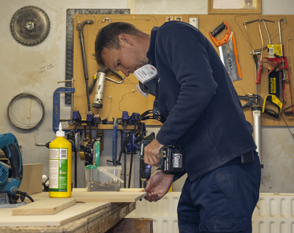 A man in a workshop using a power drill to assemble a drawer. 