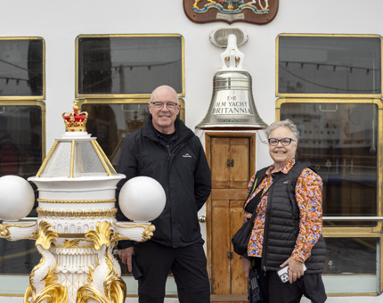 A man and a woman pose by the Bell and Binnacle on the ships deck. 