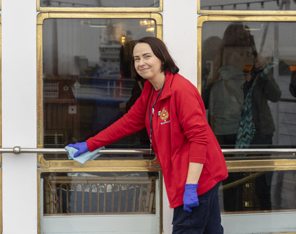 A woman wearing a red jumper polishing a handrail on the Verandah Deck.