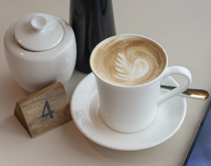 A latte and pot of sugar sitting on a table.