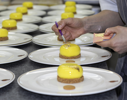 A close-up of a hand adding edible gold leaf to lemon cheesecakes. 