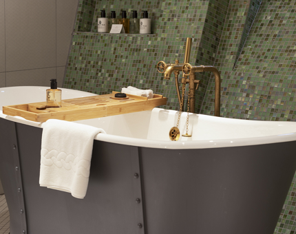 A free standing bath tub in a bathroom with green tiles.