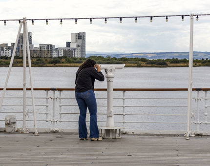 A person standing on deck looking through a telescope. 