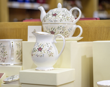 A mug, teapot and milk jug with an embroidery pattern on it, displayed in the Gift Shop. 
