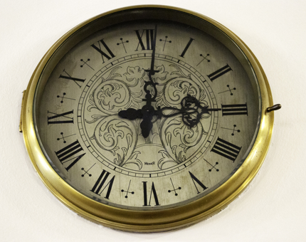 Ornate brass rimmed clock with roman numerals showing the time 3.01pm. 
