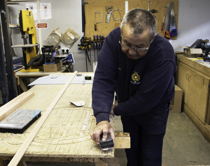 Maintenance team member sands lengths of wood to make a picture frame. 