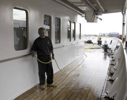 A Maintenance team member holds a hose and cleans the outside deck. 