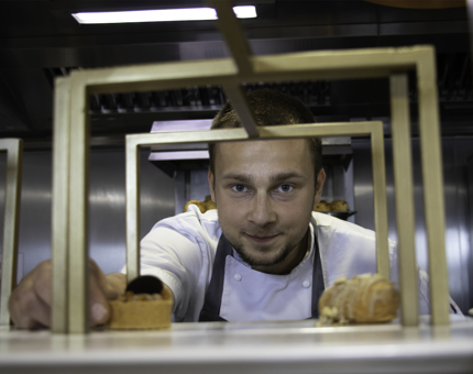 Man peers through the top tier of a cake stand as he arranges miniature pastries. 