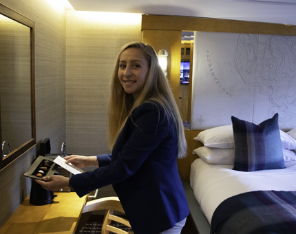 Woman places a tray of chocolates on a desk in a guest cabin. 