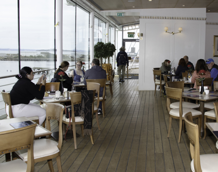 Inside the light-filled Royal Deck Tea Room with floor to ceiling windows. Visitors sit at tables enjoying lunch. 