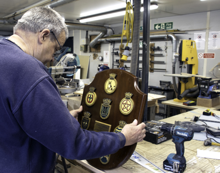 A member of the maintenance team holds a shield in the workshop while preparing a stand for it. 