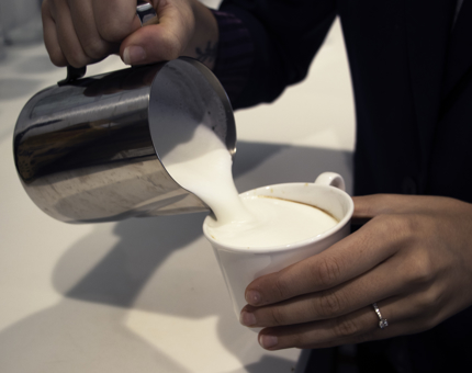 Close-up view of a Tea Room team member pouring a cappuccino into a cup. 