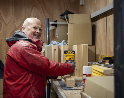 A man in a red jacket preparing wood to make planters.