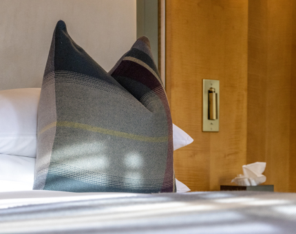 A close-up of a bed with a tartan pillow on it.