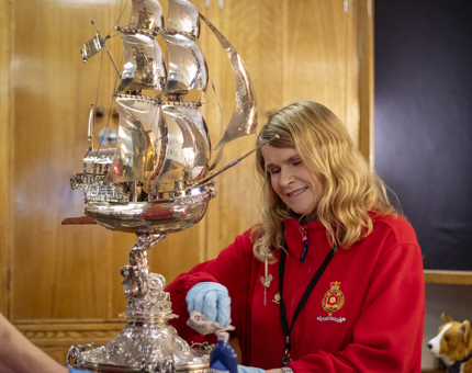 A woman wearing a red fleece polishing a silver galleon, shaped like a ship. 