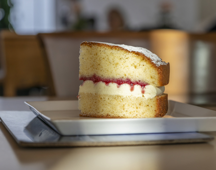 A slice of Victoria sponge cake on a white square plate sitting on a table. 