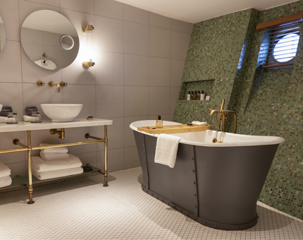 A bathroom with green tiles, a free standing bathtub and two sinks and mirrors.