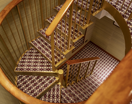 A spiral staircase with a maroon, grey and cream patterned carpet. 