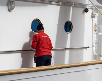 A woman in a red top cleaning the brass fittings on the port side. 