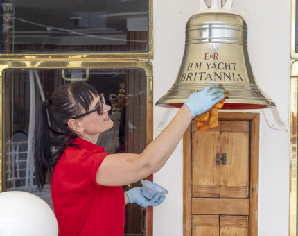 A member of the Housekeeping team is polishing The Royal Yacht Britannia's Bell. 
