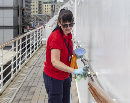 A Housekeeper polishing handrails outside on deck. 