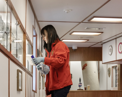 A member of the Housekeeping Team removing ornaments from a glass display case to clean in the Unwinding Room. 