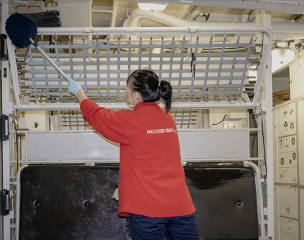A member of the Housekeeping team holding a duster as she cleans a metal bunk bed frame. 